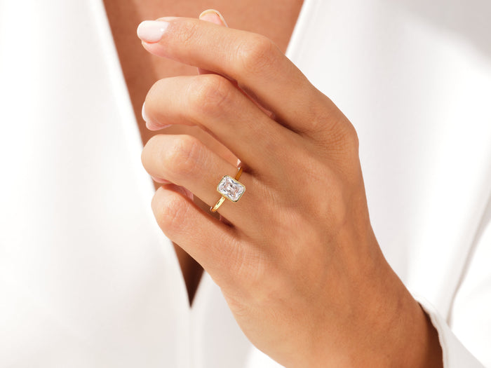 Radiant cut lab grown diamond bezel ring in yellow gold worn on the hand against a white blouse