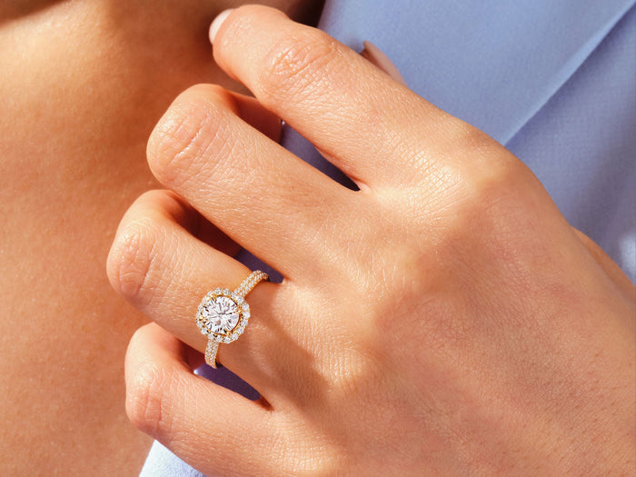 Round lab grown diamond double pave halo ring in rose gold worn on the hand at a blue shirt collar
