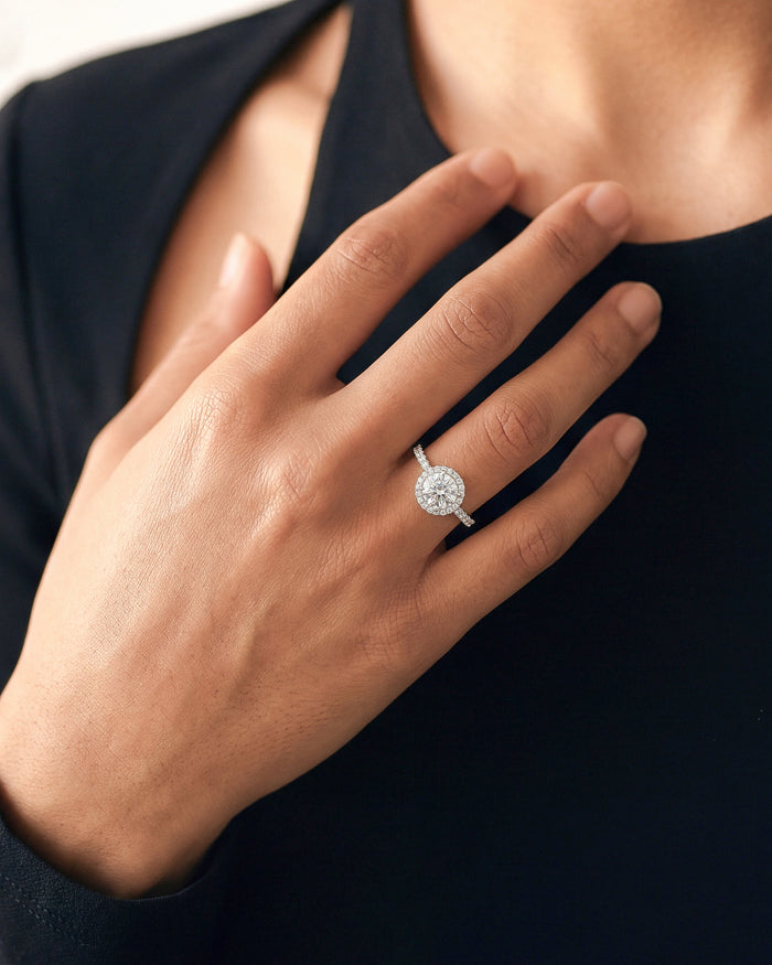 Round moissanite halo engagement ring in white gold worn on the hand at the chest