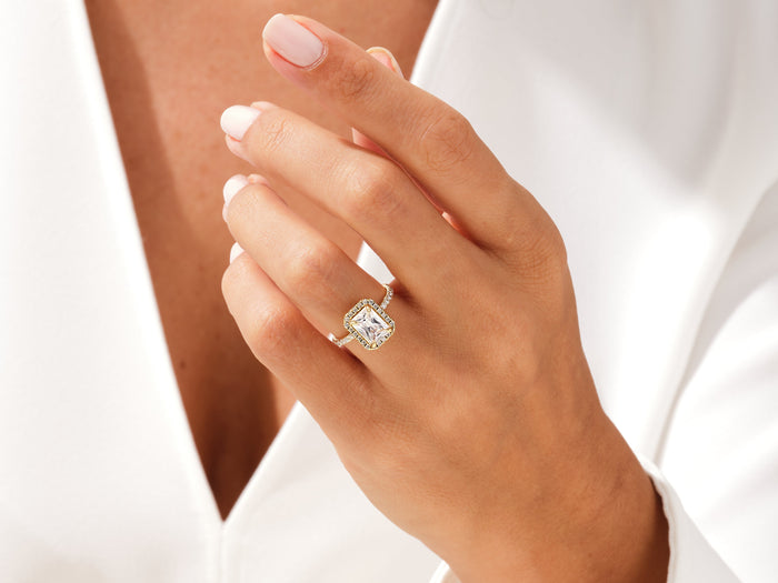 Radiant moissanite halo engagement ring in yellow gold worn on the ring finger