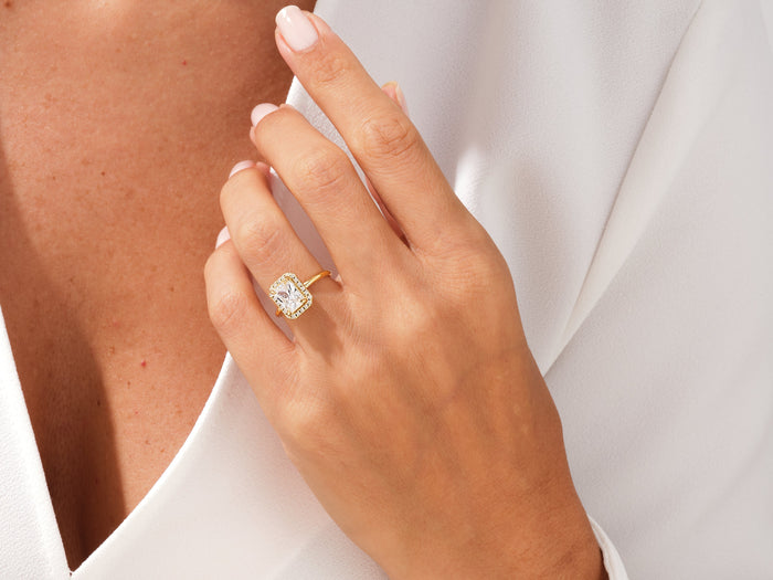 Rectangle radiant moissanite halo ring in yellow gold worn on the hand near the collar