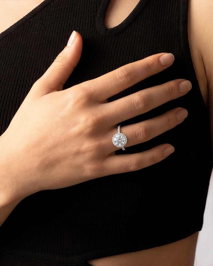 Round lab grown diamond halo pave ring in white gold worn on a hand against a black top