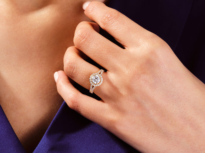 Round lab grown diamond split shank halo ring in rose gold worn on the hand against purple fabric