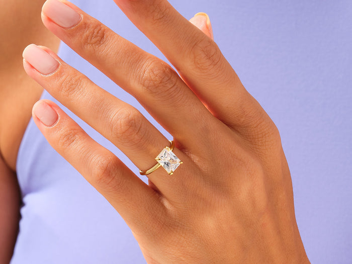 Large radiant lab grown diamond knife edge ring in yellow gold worn on the hand against lavender