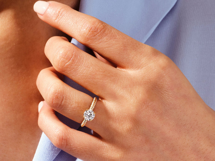 Round lab grown diamond pave knife edge ring in rose gold worn on the hand against a blue sleeve