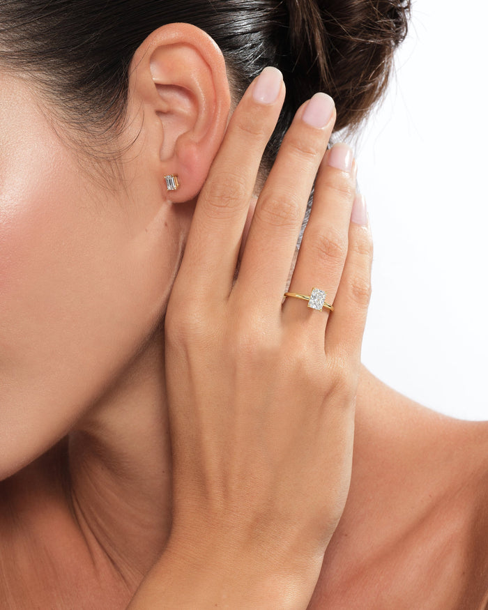 Radiant moissanite minimalist solitaire ring in yellow gold worn on the hand near the ear