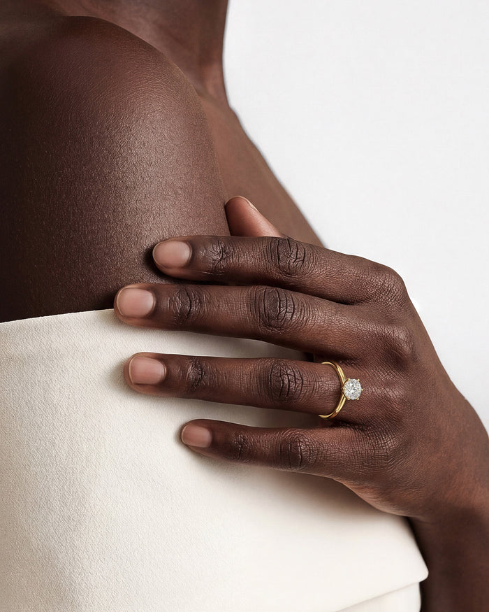 Round moissanite six prong solitaire ring in yellow gold worn on the hand against white fabric