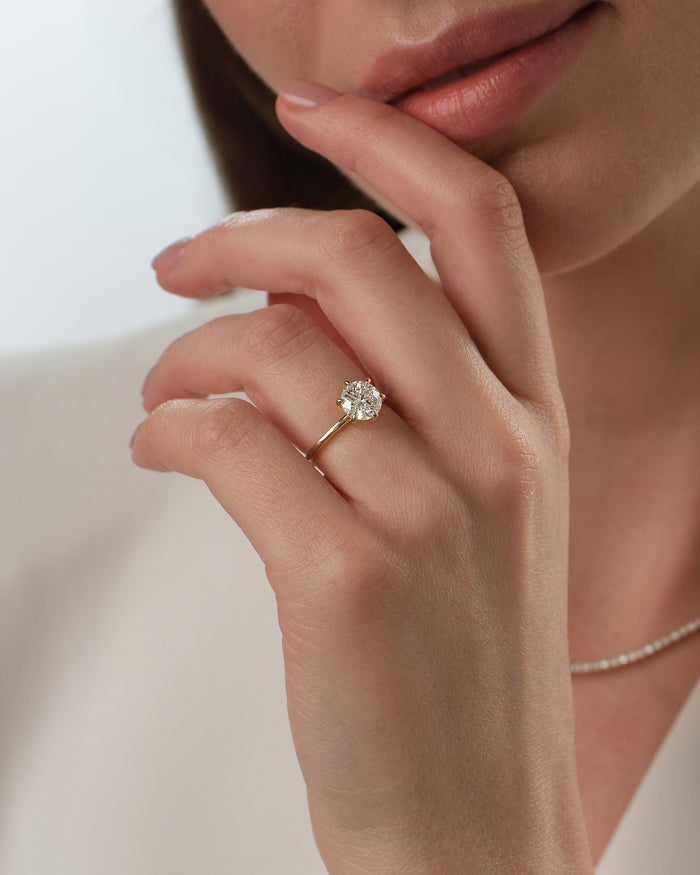 Round brilliant moissanite solitaire ring in yellow gold worn on the hand near the lips