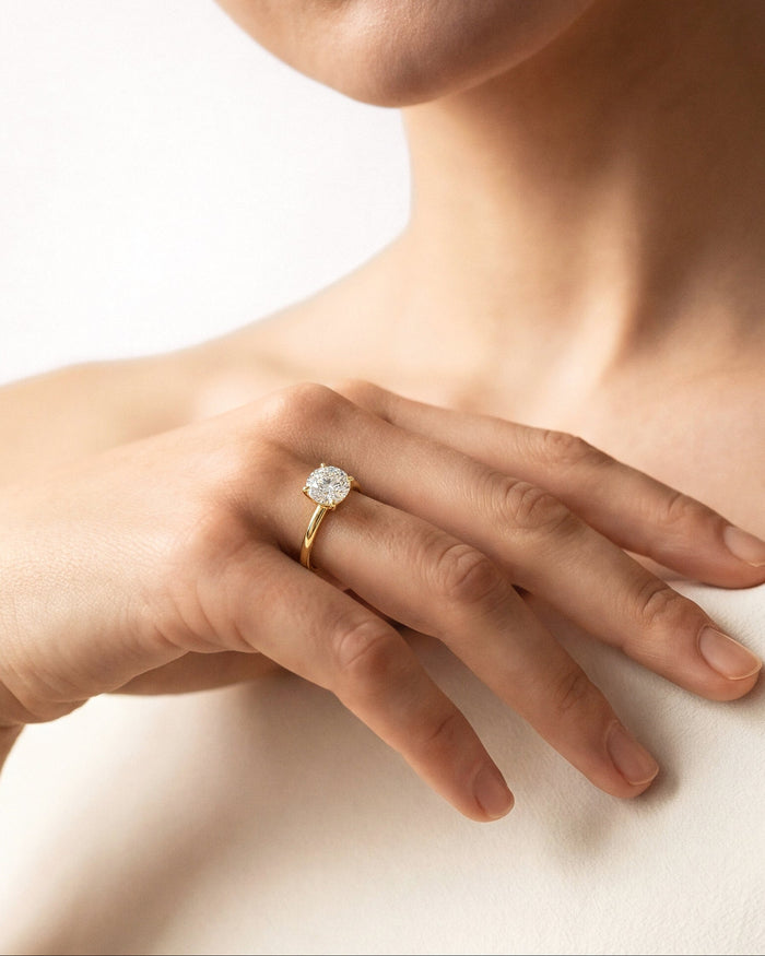 Round lab grown diamond four prong solitaire in yellow gold worn on the hand at the collarbone