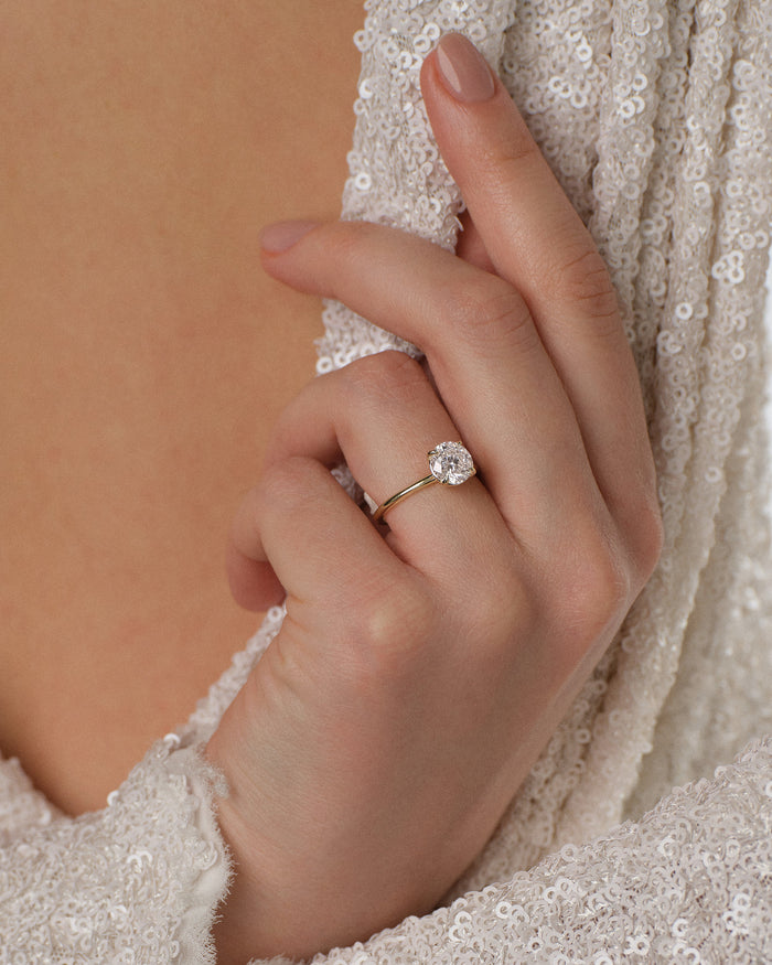 Round lab grown diamond four claw solitaire in yellow gold worn on a hand holding a sequin wrap