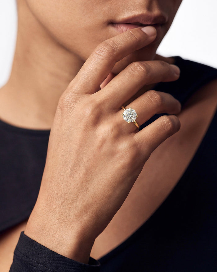 Round lab grown diamond plain band solitaire in yellow gold worn with the hand at the lips
