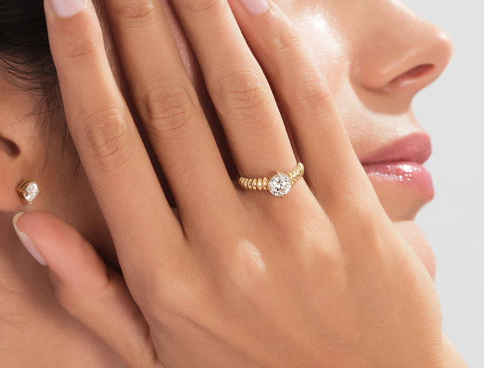 Round moissanite ribbed shoulder engagement ring in yellow gold worn on the hand near the face