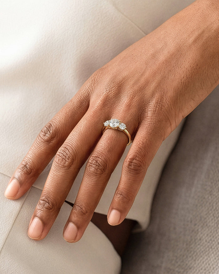 Round lab grown diamond three stone ring in yellow gold worn on the hand resting on a knee