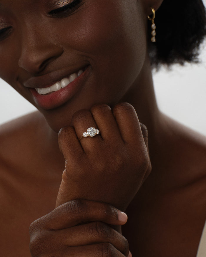 Round lab grown diamond three stone ring worn on the hand under the chin, smiling model