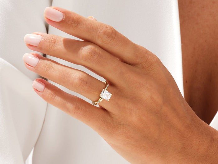 Radiant moissanite twisted band engagement ring in yellow gold worn on the ring finger