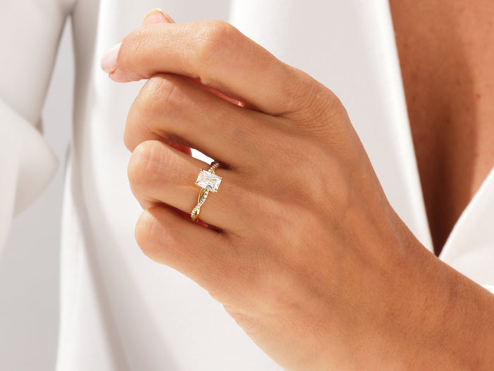 Radiant lab grown diamond twisted engagement ring in yellow gold worn on a hand against a white shirt