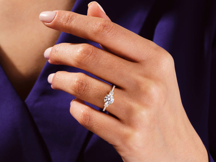 Round lab grown diamond three stone ring in rose gold worn on the hand against a purple sleeve