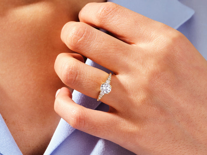 Round lab grown diamond graduated side stone ring in yellow gold worn on the hand at a lilac collar