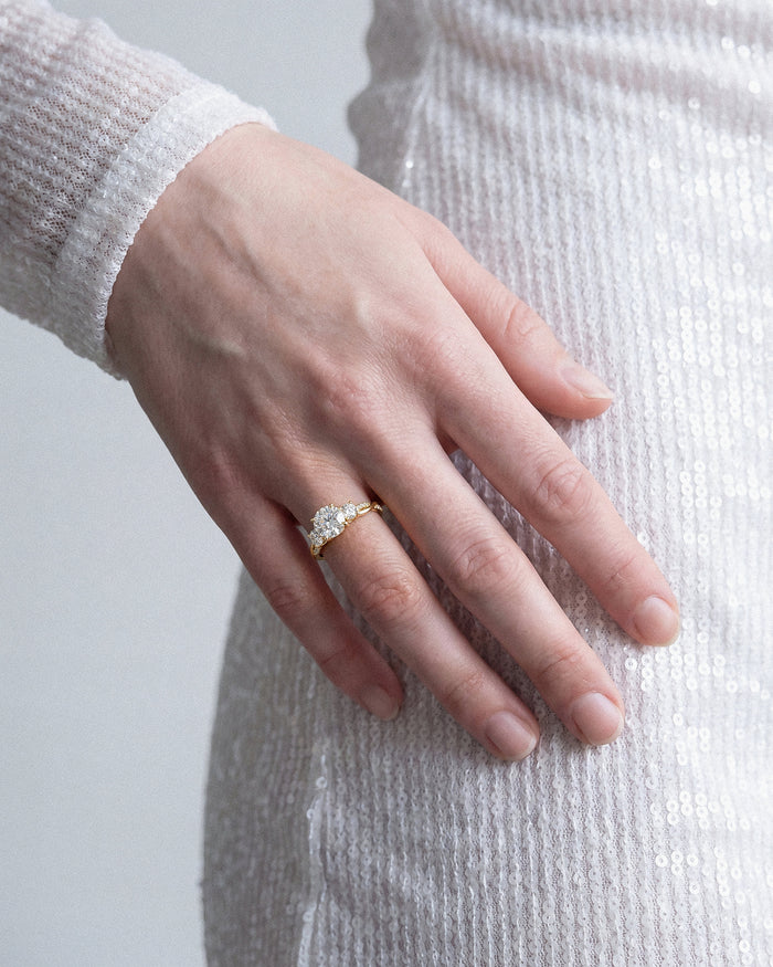 Round lab grown diamond three stone twisted vine ring in yellow gold worn on the hand against a sequined dress