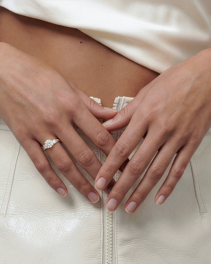 Round lab grown diamond three stone twist band ring worn on the hand with hands folded at the waist