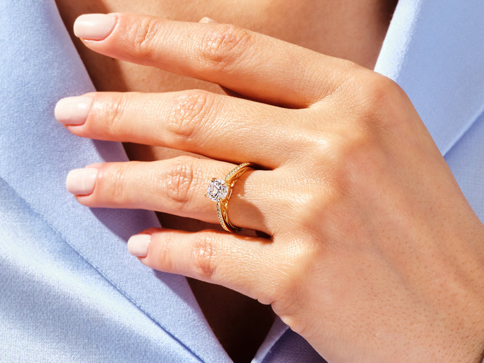 Round moissanite vintage milgrain ring in yellow gold worn on the hand against a blue shirt