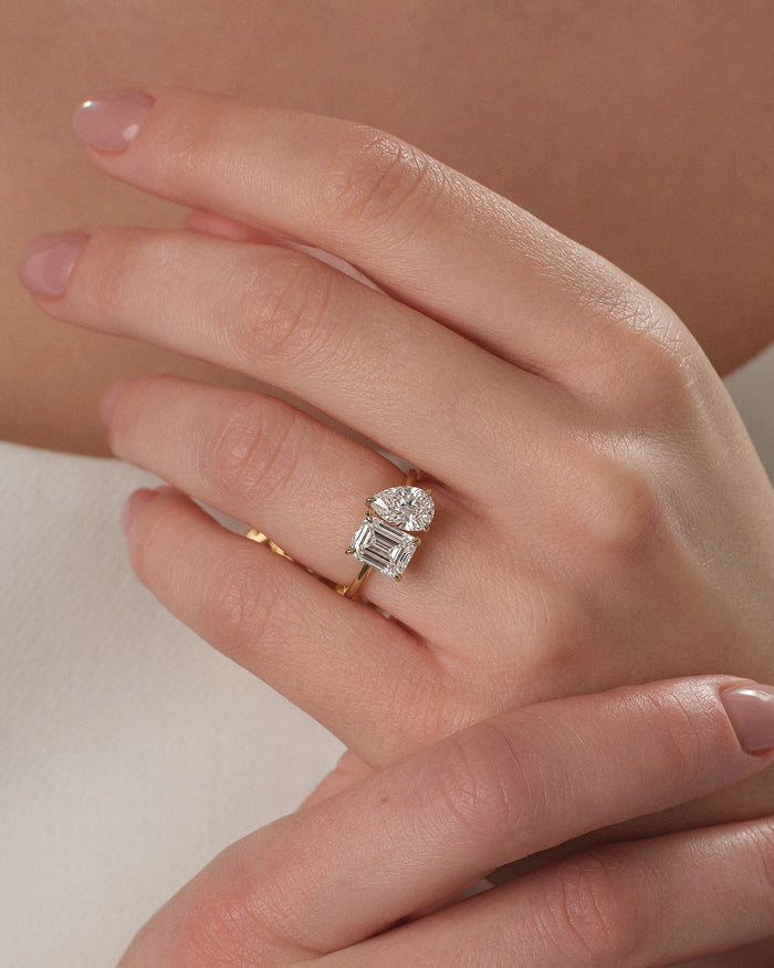 Emerald and pear lab grown diamond toi et moi ring in yellow gold worn on a relaxed hand, close up