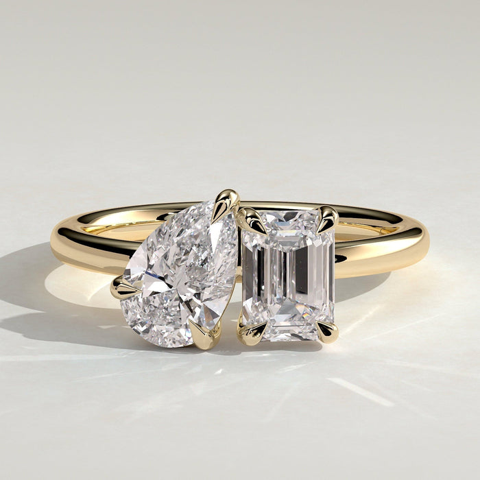 Pear and emerald cut moissanite toi et moi engagement ring on a rounded yellow gold band