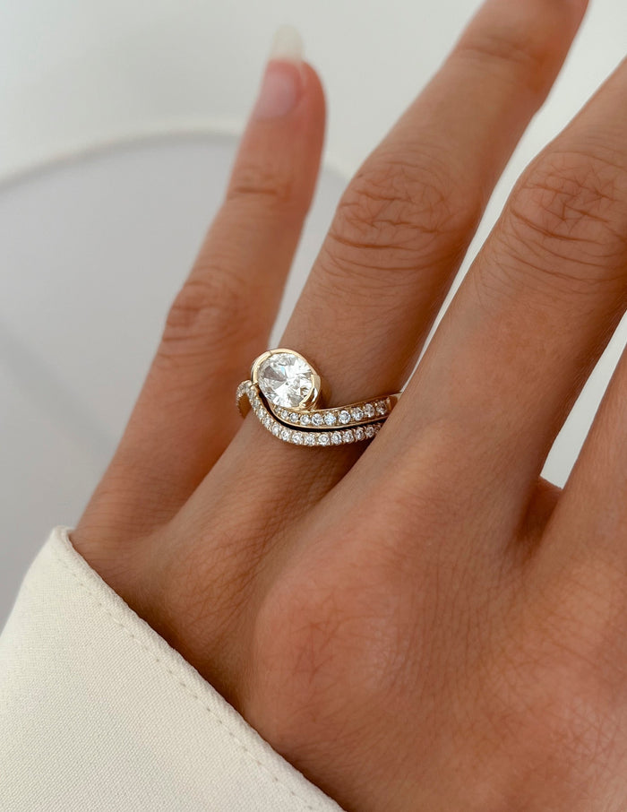 Angled view of east-west oval lab grown diamond bridal set with two rows of pave stones on the hand