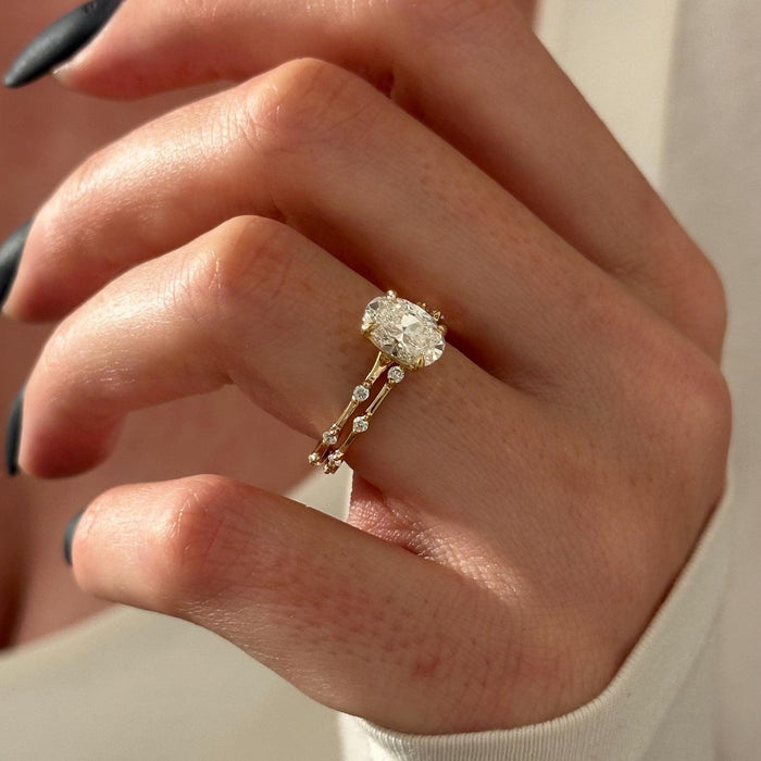 Angled view of oval moissanite solitaire with small stones spaced along thin gold bands