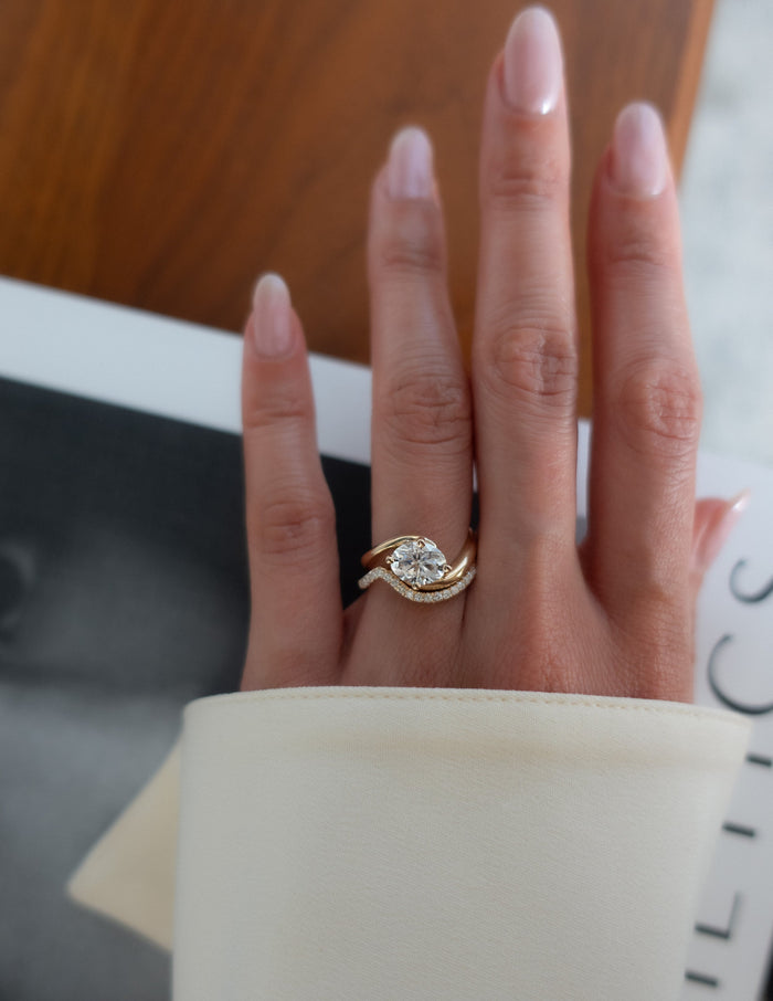 Oval moissanite swirl engagement ring and curved pave wedding band in yellow gold on the hand