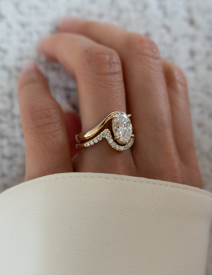 Oval moissanite swirl bridal set in yellow gold with curved pave band, angled view on the hand