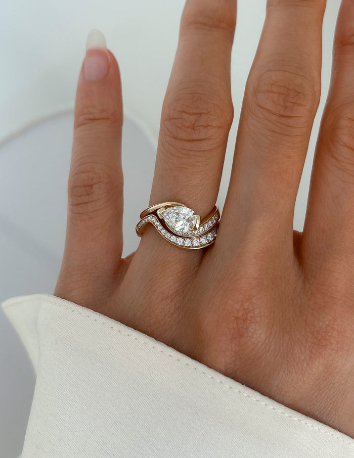 Pear lab grown diamond bypass engagement ring with pave lower arm and wide pave wedding band, top view on the hand