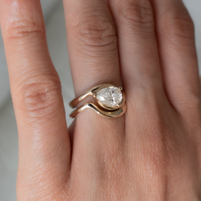 Close-up of pear lab grown diamond set sideways in a swirl bypass ring with a plain curved gold band