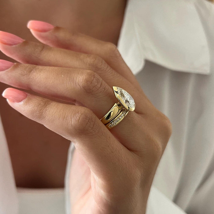 Side view of pear moissanite bezel ring showing the wide polished shank and stone set band