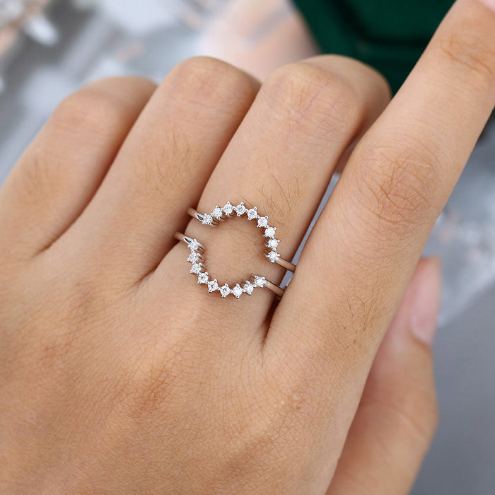 Round moissanite double curved prong wedding band, worn on the finger in white gold