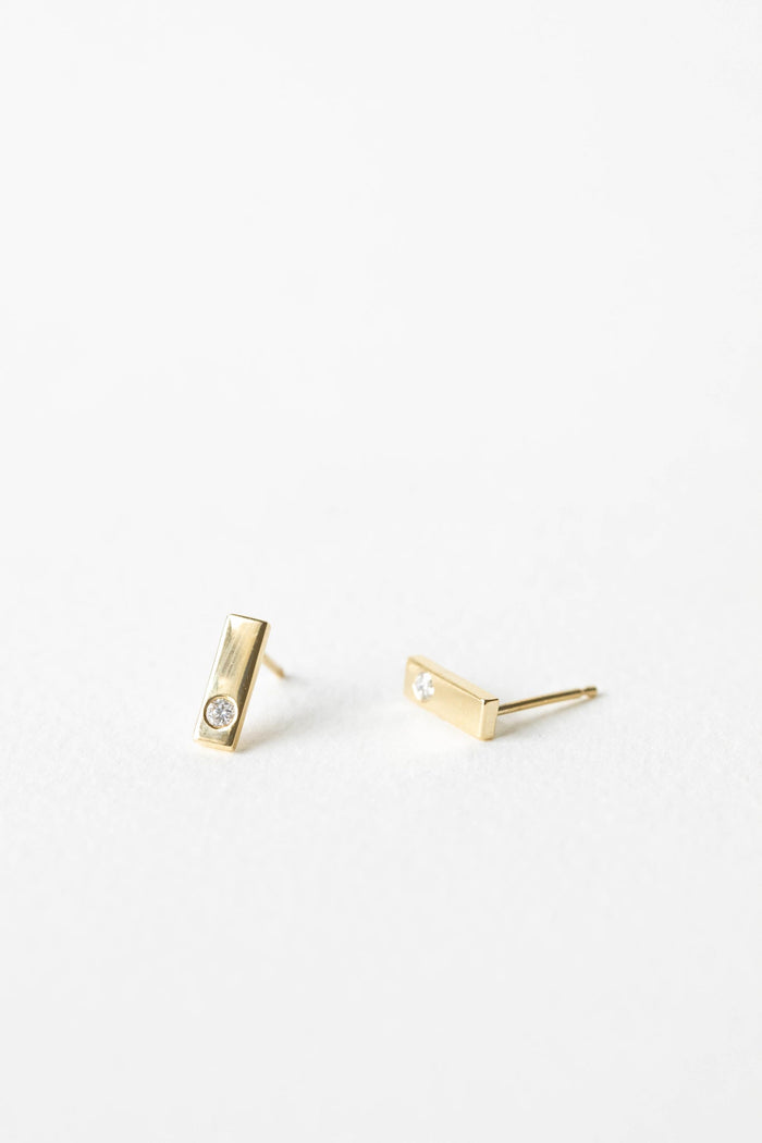Pair of polished yellow gold bar stud earrings, each flush set with a small round lab grown diamond, on a white background