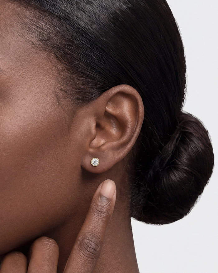 Model wearing round milgrain bezel solitaire lab grown diamond stud earrings, close up on the ear