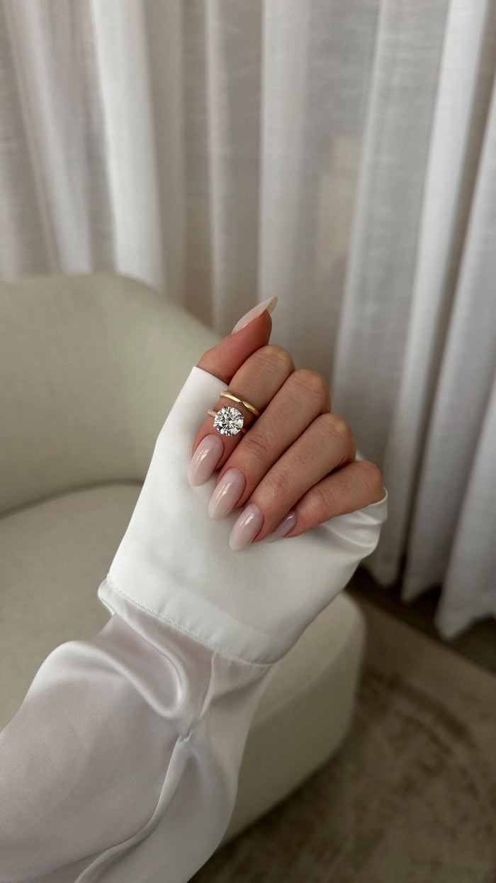 Round moissanite solitaire bridal set in yellow gold with white prong head on a raised hand
