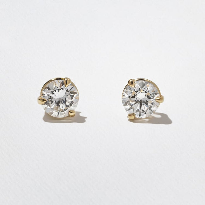 Front view of round lab grown diamond solitaire stud earrings in three prong yellow gold settings on white paper