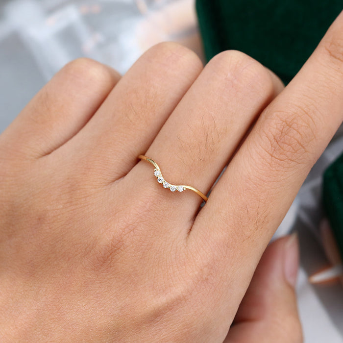 Round moissanite wave curved wedding band, worn on the finger in yellow gold