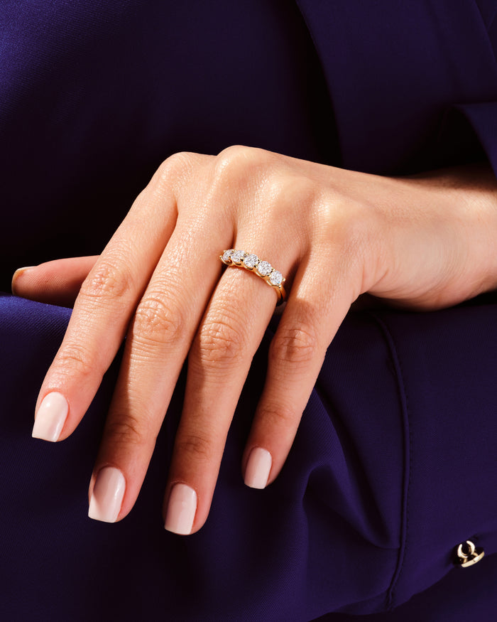 Five stone moissanite anniversary band in yellow gold worn on a hand