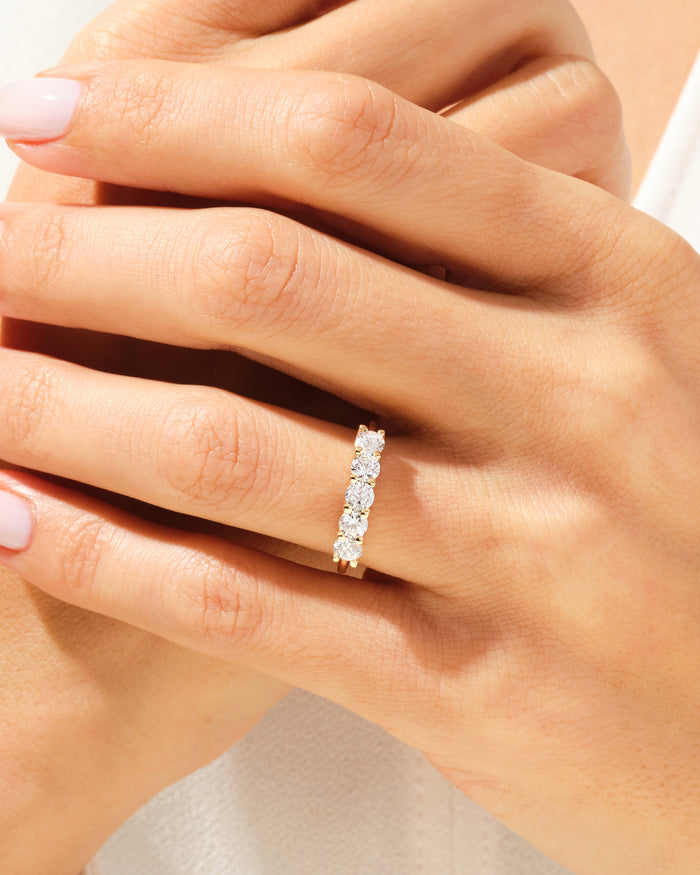 Five stone moissanite anniversary band in yellow gold worn on a hand