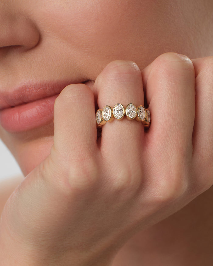 Wide oval bezel eternity band in yellow gold worn on the finger, close view