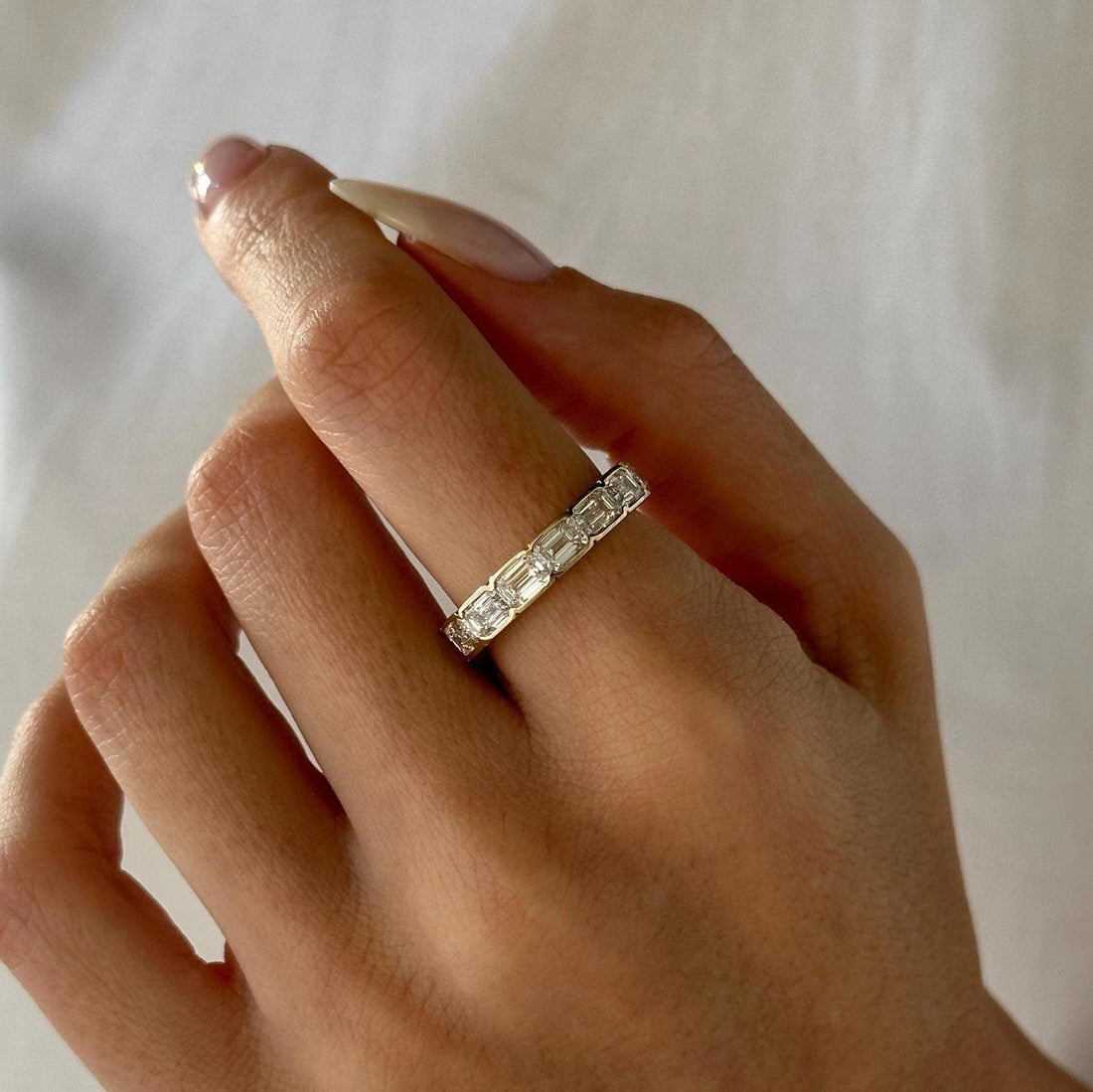 Emerald cut lab grown diamond bezel set full eternity band in yellow gold worn on a finger