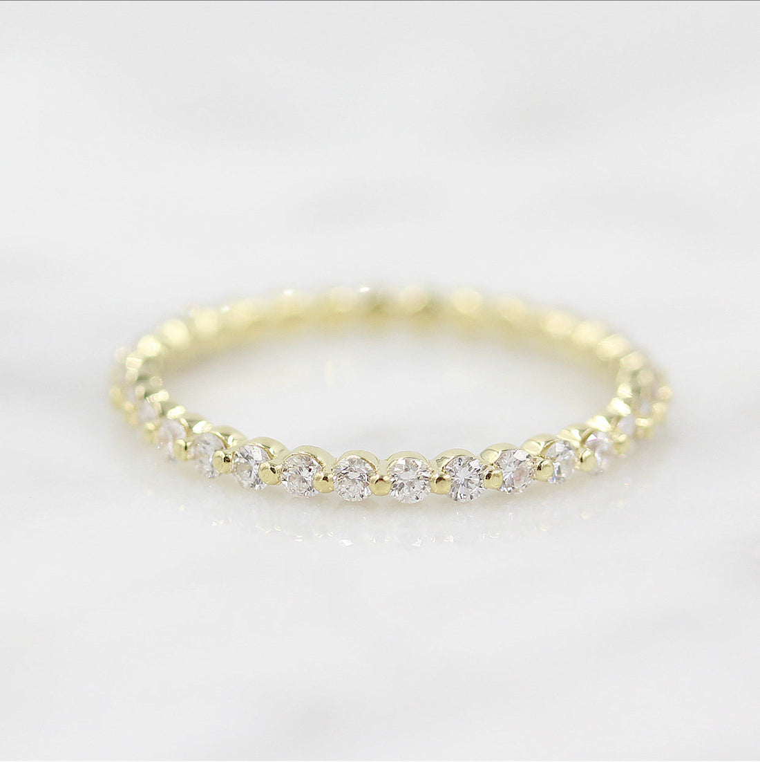 Round lab grown diamond wedding band in yellow gold on a marble surface