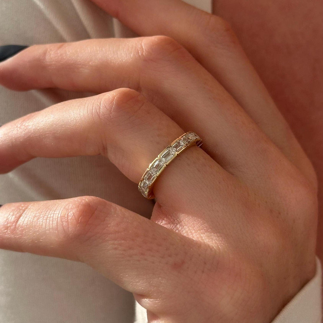 Emerald cut lab grown diamond bezel set full eternity band in yellow gold worn on a finger