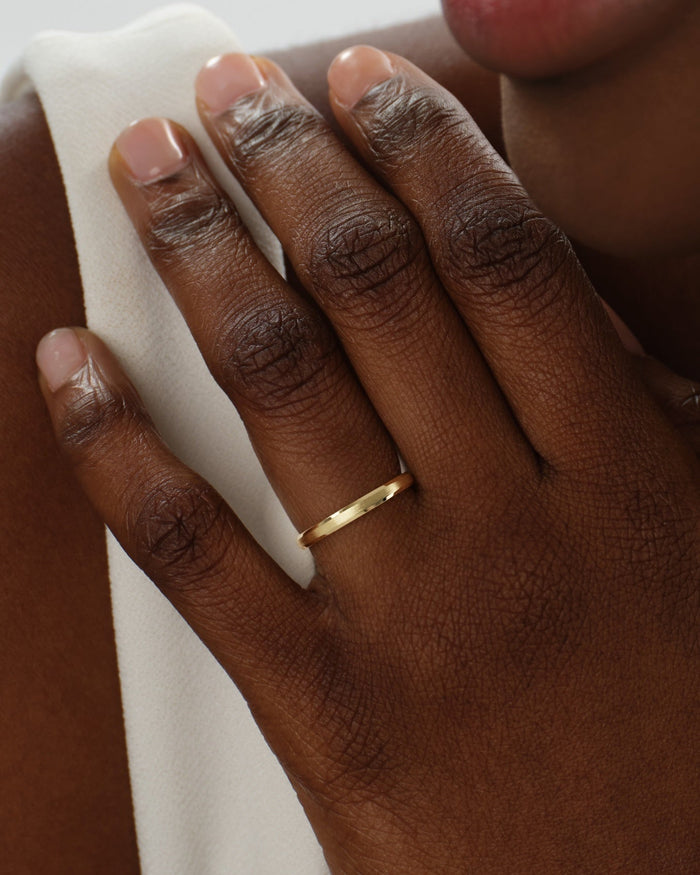Hand wearing a 2mm matte brushed gold wedding band against a white top