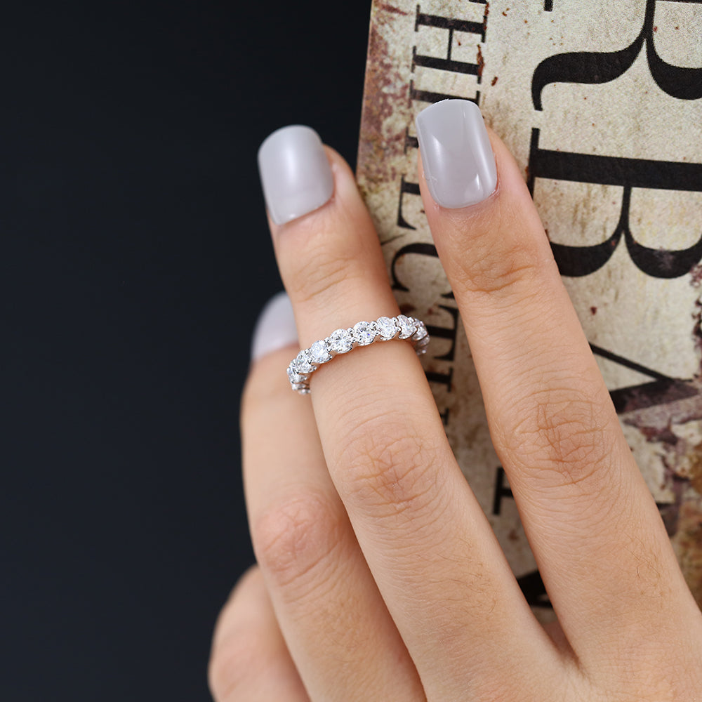 White gold round moissanite full eternity band worn on a finger holding a book