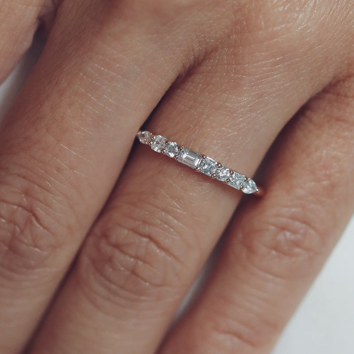 Slim mixed shape moissanite half eternity wedding band in rose gold worn on a finger, close view