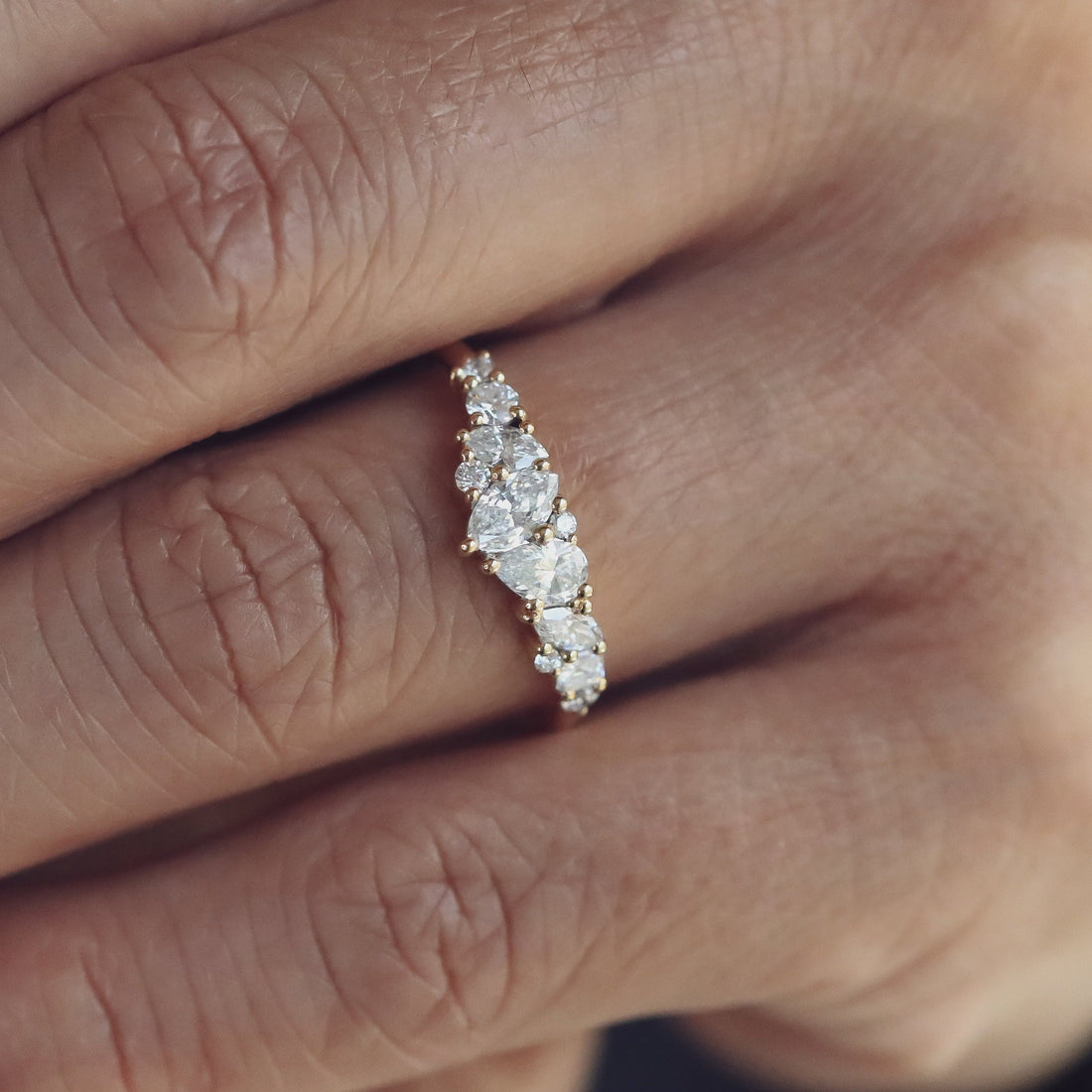 Close up of a mixed shape lab grown diamond cluster wedding band in yellow gold on a finger